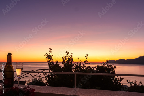 Champagne bottle with scenic sea view during sunset from luxury apartment on Mediterranean Sea. Terrace balcony with arch overlooking the coastline in Praiano, Amalfi Coast, Campania, Italy, Europe