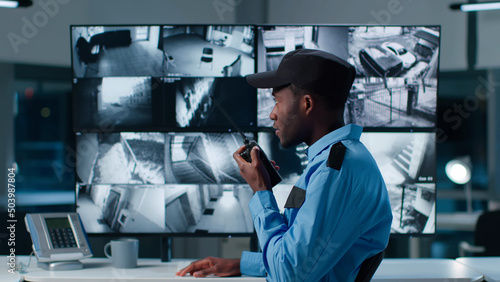 Fotografia African-American security officer watching the screens talking on radio in contr