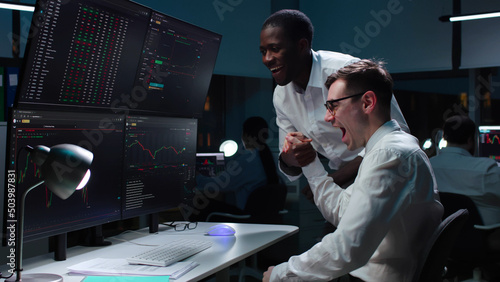 Fotografie Diverse traders celebrate success looking at monitors with data working late