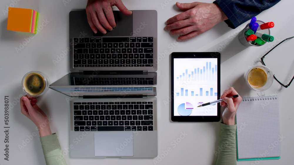Top view of financial specialists discuss sales chart on digital tablet Top view of financial specialists discuss sales chart on digital tablet