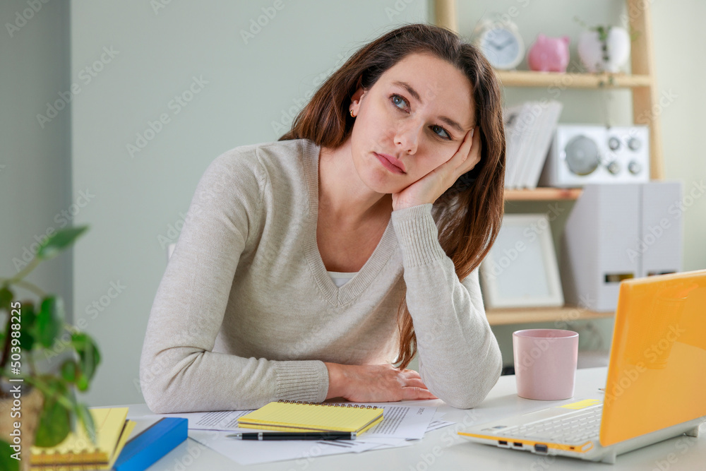 Young freelancer woman has tired look in home office, online work at laptop on the white table Young freelancer woman has tired look in home office, online work at laptop on the white table