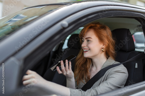 Close-up of woman using mobile phone and talking on the speaker while driving car. Woman talking on in-car speakerphone while driving