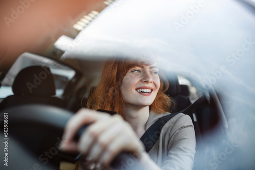 Foto Beautiful smiling young redhead woman behind steering wheel driving car