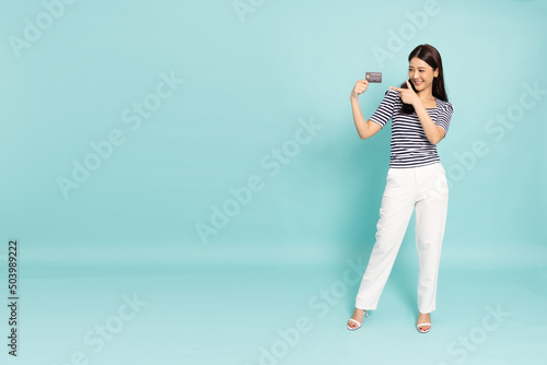 Happy young Asia businesswoman smiling, showing and pointing credit card for paying online business isolated on green background, Full body composition © comzeal