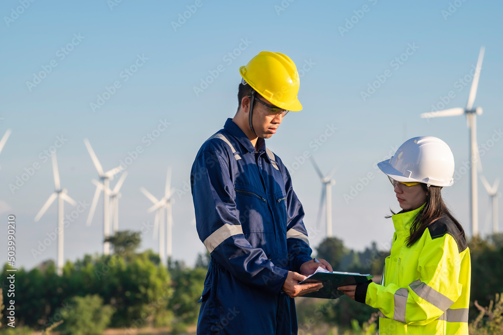 Two engineers working and holding the report at wind turbine farm Power Generator Station on mountain,Thailand people,Technician man and woman discuss about work Two engineers working and holding the report at wind turbine farm Power Generator Station on mountain,Thailand people,Technician man and woman discuss about work