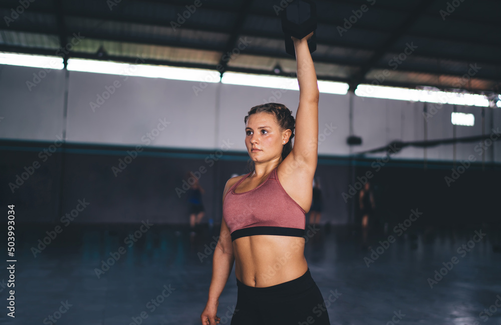 Caucasian female lifting dumbell for keeping body in tonus - reaching fitness goals, strong athletic woman spending time in gym using sportive equipment for feeling wellness and vitality motivation