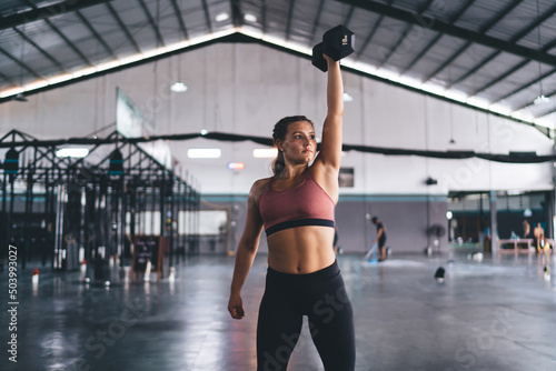 Caucasian female lifting dumbell for keeping body in tonus - reaching fitness goals, strong athletic woman spending time in gym using sportive equipment for feeling wellness and vitality motivation