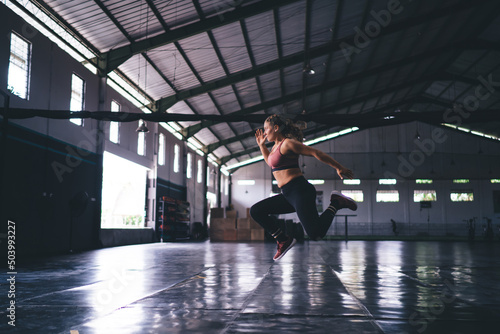 Side view of determined female athlete jumping with tough during cardio workout training in sportive gym studio, motivated woman in active wear slimming for keeping body shape in tonus - crossfit © BullRun