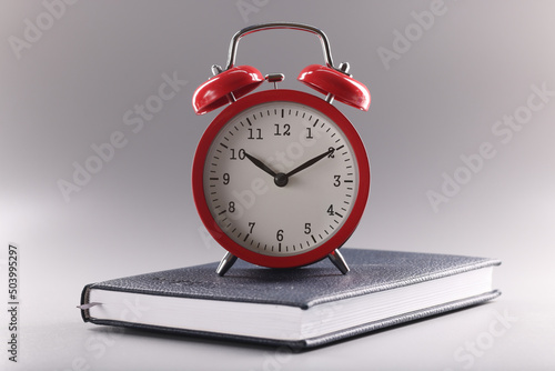 Red retro clock stand on top of closed book or diary, time to study, time to learn new information