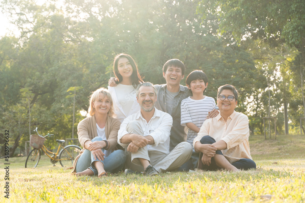 Fototapeta premium Portrait group of diversity people sitting on grass and taking photo together. Caucasian senior couple with Asian family at park