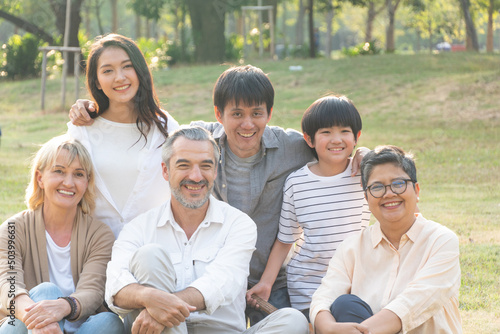 Portrait group of diversity people sitting on grass and taking photo together. Caucasian senior couple with Asian family at park