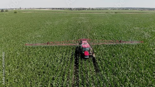 A tractor sprayer sprays corn in the field. Shooting from a 4K drone. Spraying of chemical fertilizers on an agricultural field