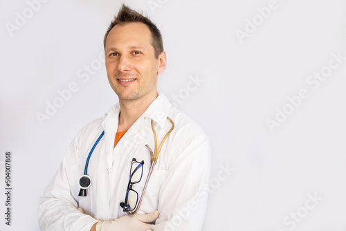 Close-up headshot of smiling young male doctor wearing white coat, isolated on gray background © Mykola