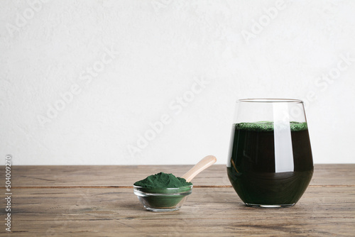 fresh green drink with spirulina in glass, spirulina powder with spoon on wooden background. useful habits, self care and healthy lifestyle.copy space