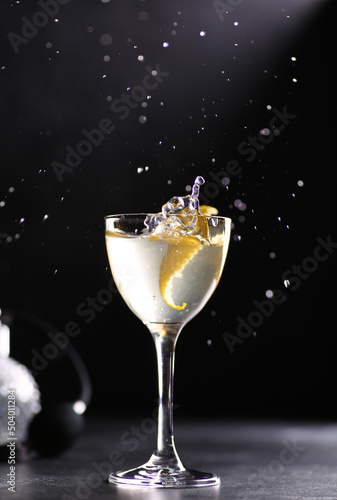 Drinks and cocktails. Light beverage with ice  lemon twist in a large transparent glass on black table  splash. Restaurant  bar. Background image  copy space