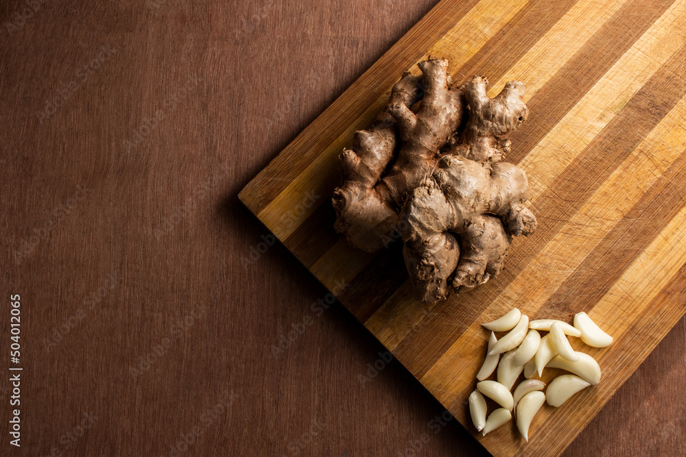 Ginger roots and garlic in a wooden cutting board. wooden background Ginger roots and garlic in a wooden cutting board. wooden background