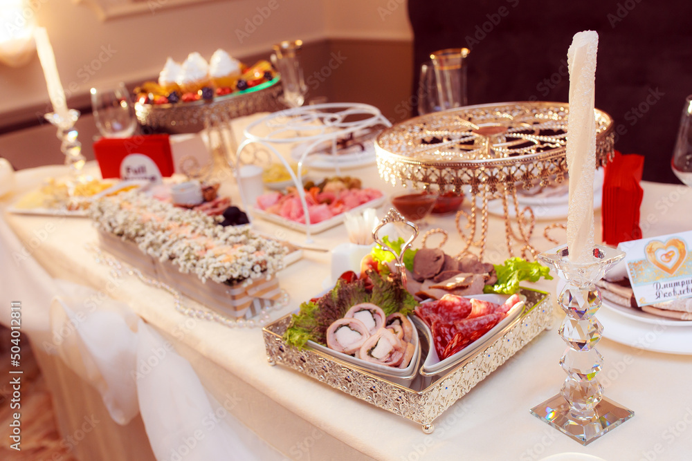 Cheese slices, fruit platter, cold cuts on a served festive table. Decor from natural flowers of the wedding table.