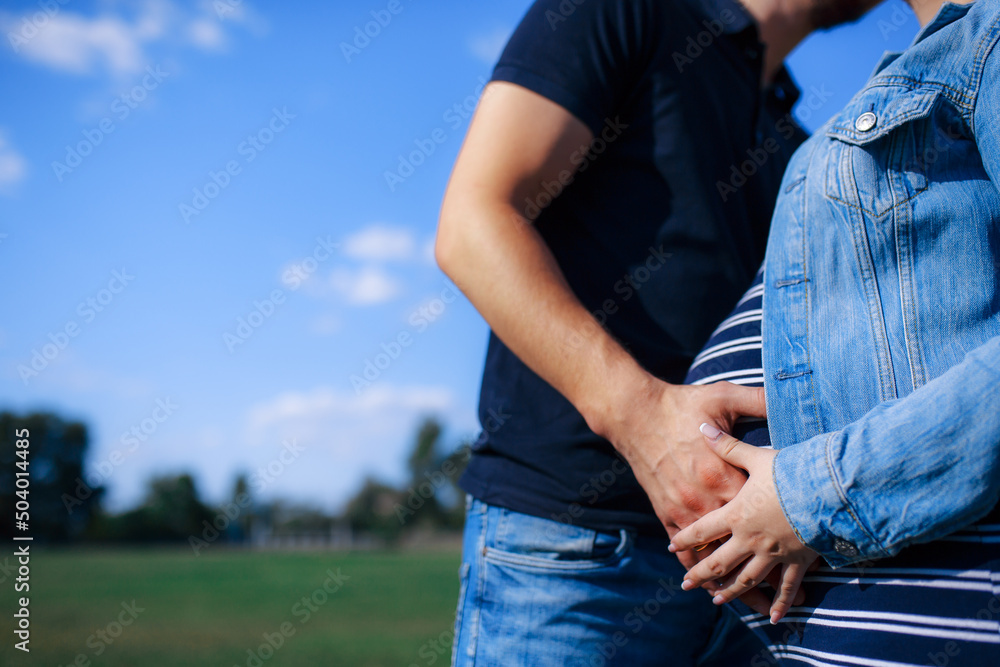 A pregnant woman in the arms of her husband. Summer sunny weather. A couple in love are hugging.