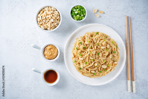 Wheat pasta with peanut butter soy sauce, roasted peanuts and scallion in a plate