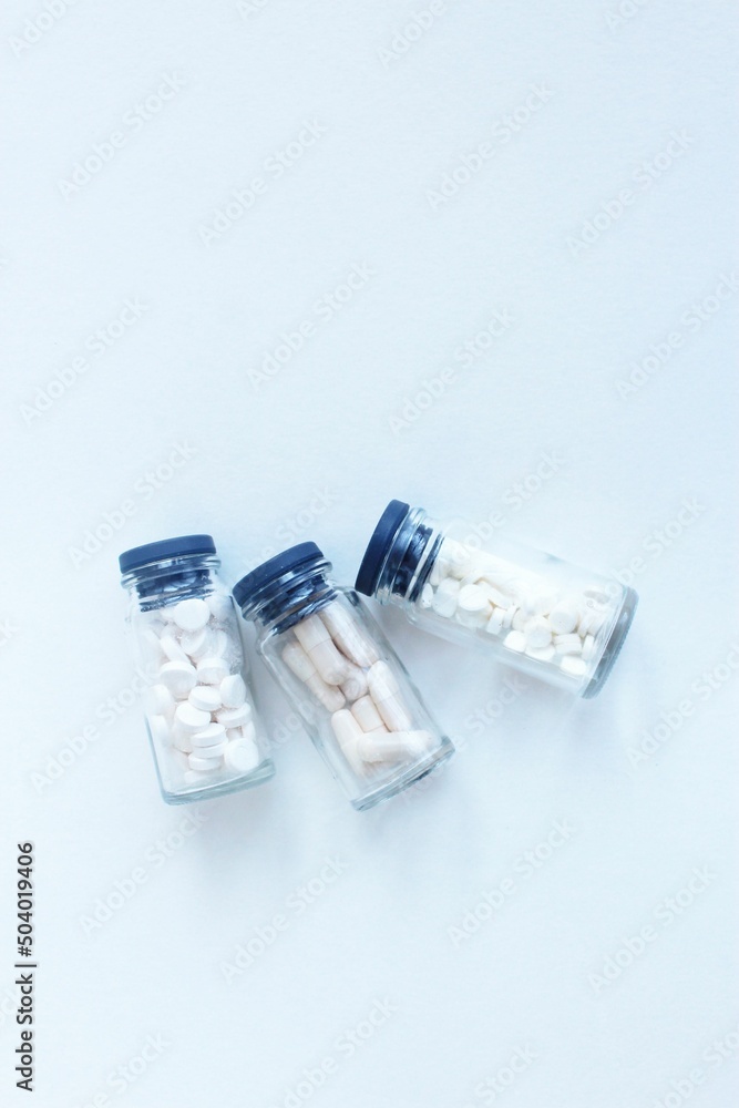 Three transparent glass vials with white tablets on a white background. Vitamins and medicines. Three transparent glass vials with white tablets on a white background. Vitamins and medicines.