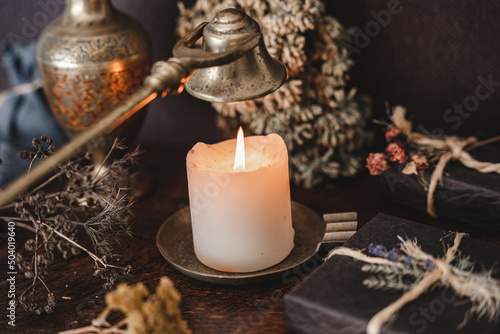 Wiccan witch putting out a white candle flame with antique brass gold colored wick snuffer. Casting a spell at a witch's altar photo