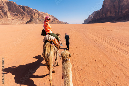 beautiful young woman tourist in white dress riding on camel in wadi rum desert, Jordan © minoandriani