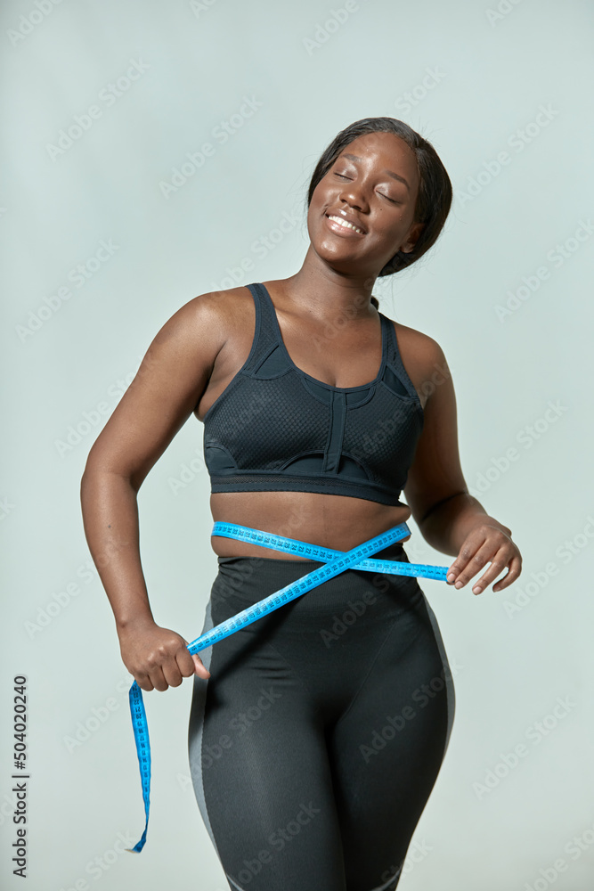 Φωτογραφία Happy african american young woman measuring waist size with tape measure