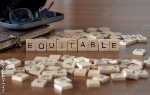 equitable word or concept represented by wooden letter tiles on a wooden table with glasses and a book photo