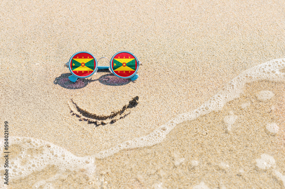 Naklejka premium Sunglasses with flag of Grenada State on a sandy beach. Nearby is a sea lightning and a painted smile. The concept of a successful vacation in the resorts of Grenada.