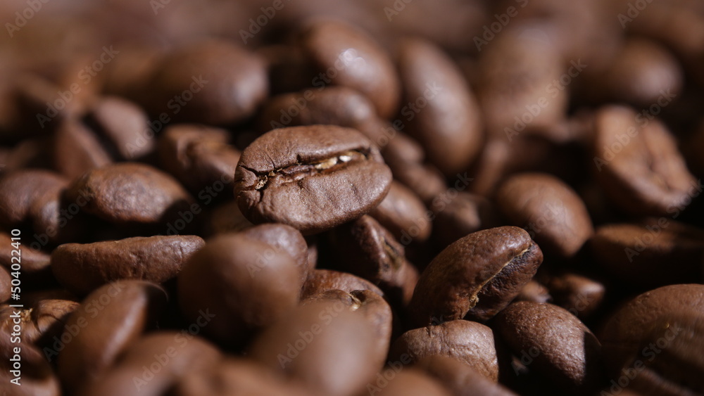 Naklejka premium close-up on a coffee bean that is among other grains in the dark