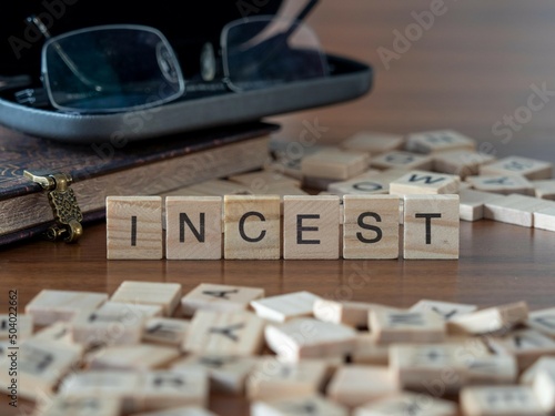 incest word or concept represented by wooden letter tiles on a wooden table with glasses and a book photo