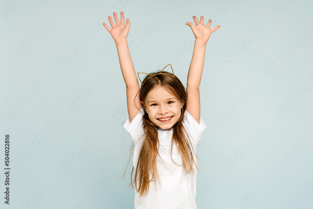 Portrait of a young excited crazy smiling girl in cat ears raising her hands in joy and looking at the camera on a blue background Portrait of a young excited crazy smiling girl in cat ears raising her hands in joy and looking at the camera on a blue background