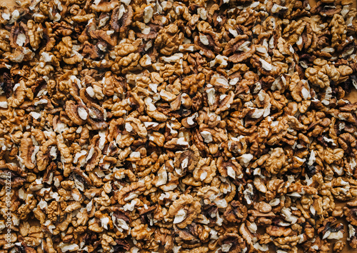 Background, texture of many brown pieces of walnuts, peeled nuts lying on the table. Food photography, top view.