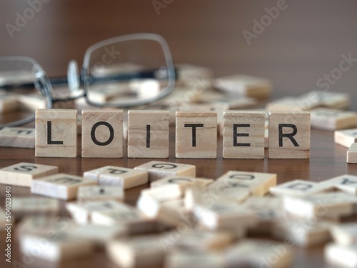 loiter word or concept represented by wooden letter tiles on a wooden table with glasses and a book