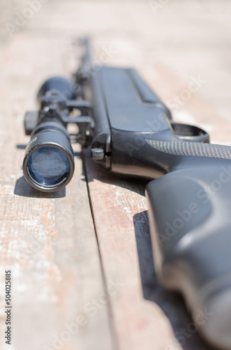 A sniper rifle with an optical sight lies on a worn wooden board. Weapon with an optical sight. Weapon deliveries. Selective focus.