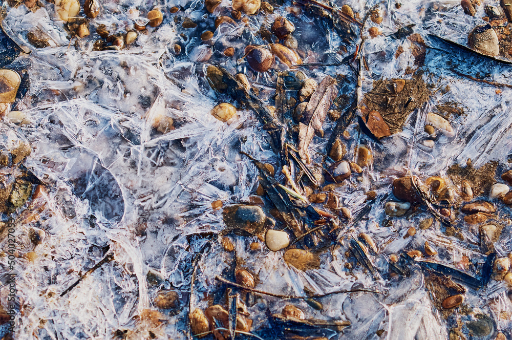 Thin ice in the morning on a rocky beach. Sunrise. Night frosts. Close view. Natural abstract texture. Changeable weather in spring. Thin ice in the morning on a rocky beach. Sunrise. Night frosts. Close view. Natural abstract texture. Changeable weather in spring.