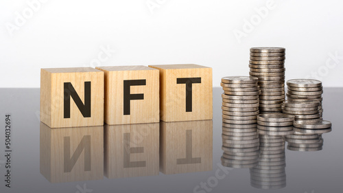 NFT - text on wooden cubes on a cold grey light background with stacks coins