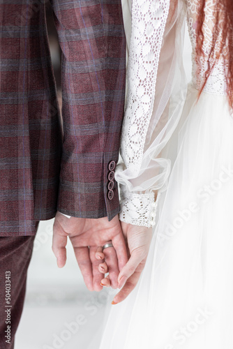 Beautiful red-hair bride in a white wedding dress and bouquet of flowers wearing pearls and a handsome groom with a red beard in a suit. Young loving couple holding hands