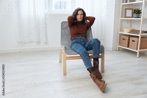 Upset frustrated thoughtful curly adorable woman hold hands behind head lost in sad thoughts about irreparable mistake decision about divorce sit in chair at home looks aside. Heavy thoughts concept