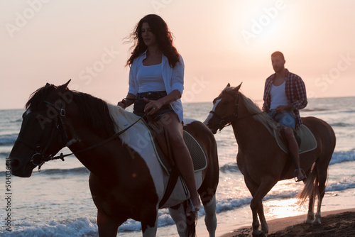 a loving couple in summer clothes riding a horse on a sandy beach at sunset. Sea and sunset in the background. Selective focus 