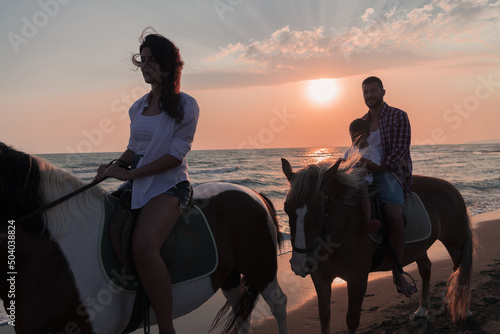 The family spends time with their children while riding horses together on a sandy beach. Selective focus 