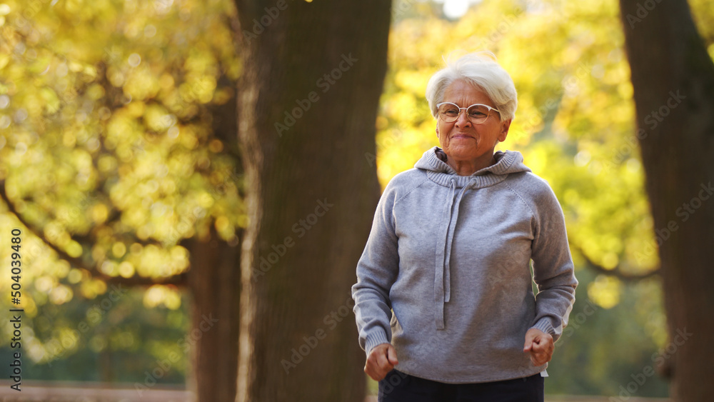 Jogging in park. Retired gray-haired caucasian lady in gray hoodie runs around her favorite park. Wellbeing concept. High quality photo Jogging in park. Retired gray-haired caucasian lady in gray hoodie runs around her favorite park. Wellbeing concept. High quality photo