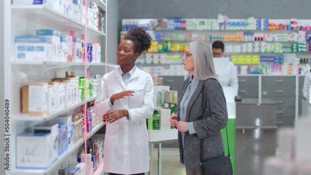 Confident african american female pharmacist showing medical devices to aged woman on drugstore showcase. Concept of people, consultation and pharmaceutics. Confident african american female pharmacist showing medical devices to aged woman on drugstore showcase. Concept of people, consultation and pharmaceutics.
