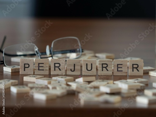 perjurer word or concept represented by wooden letter tiles on a wooden table with glasses and a book photo