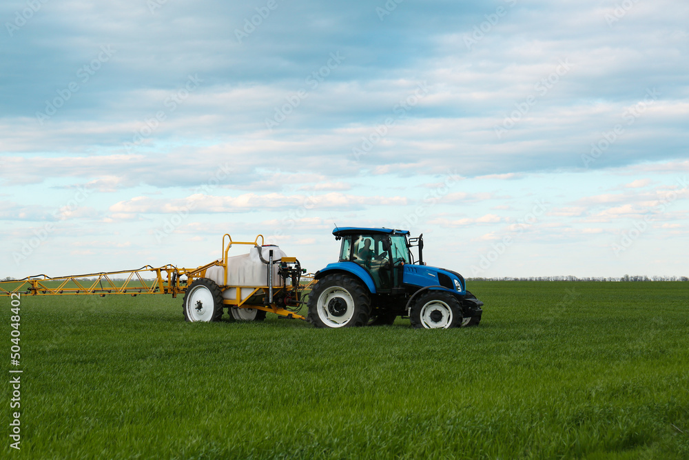 Tractor spraying pesticide in field on spring day. Agricultural industry