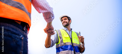 Handsome European engineers greet each other with fist bumps. Middle Eastern workers smiling with confidence, happy at work, professional, wearing PPE,hard hat,reflective,vest.New normal professional