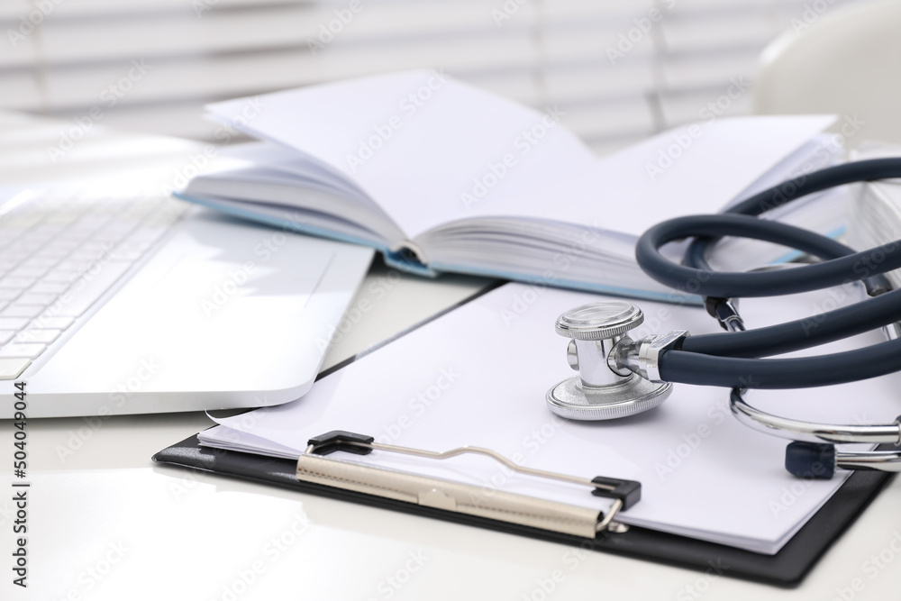Book, stethoscope, laptop and clipboard on white table indoors. Medical education Book, stethoscope, laptop and clipboard on white table indoors. Medical education