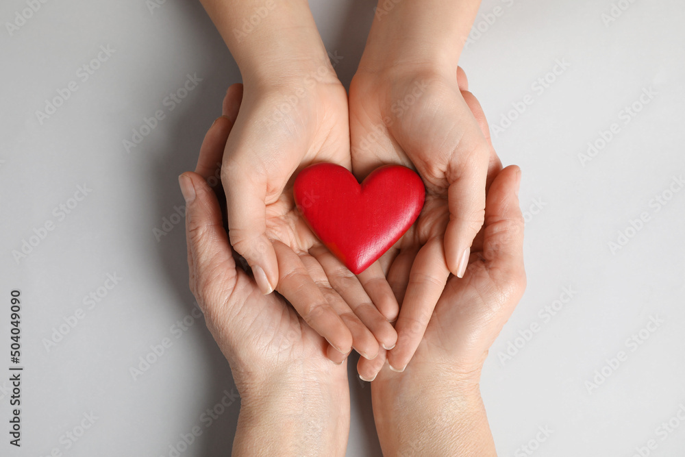 Obraz premium Young and elderly women holding red heart on light grey background, top view