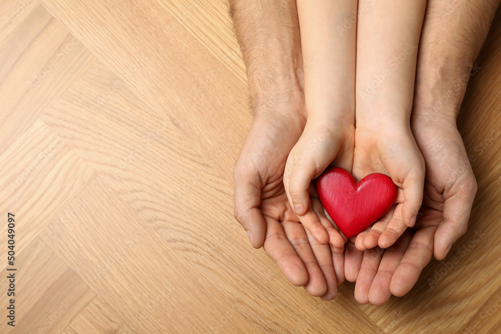 Man and kid holding red heart in hands at wooden table, top view. Space for text Man and kid holding red heart in hands at wooden table, top view. Space for text