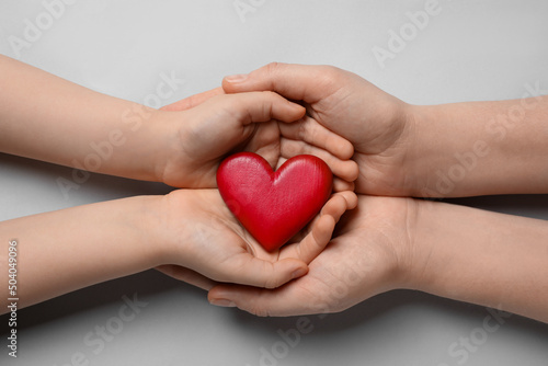 Woman and kid holding red heart in hands on light grey background, top view